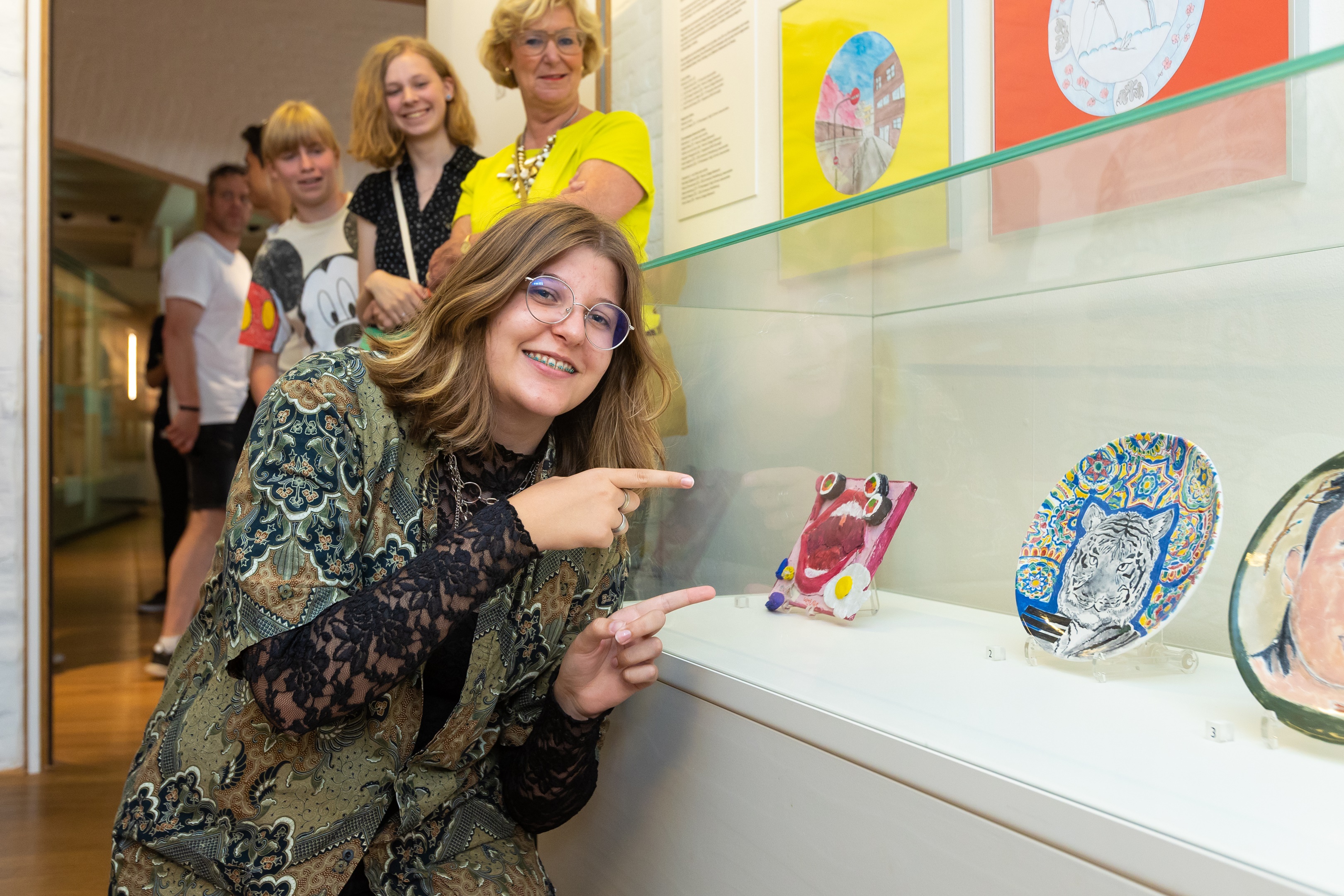 Een winnaar van de ontwerpwedstrijd 2022 wijst blij naar haar kunstwerk. Foto door Marieke Balk Fotografie